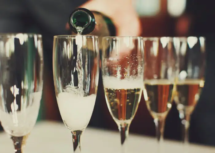 Close up of row of champagne glasses being filled by a bottle