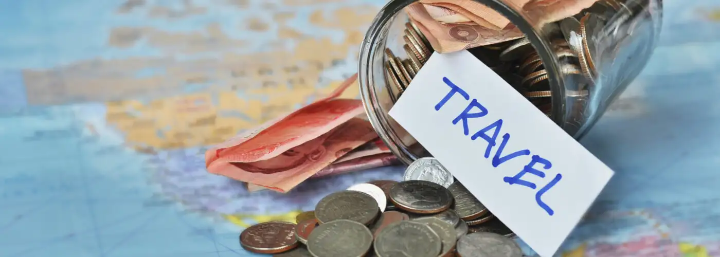 Jar of cash and coins tipped over on a world map with a label that says "travel"