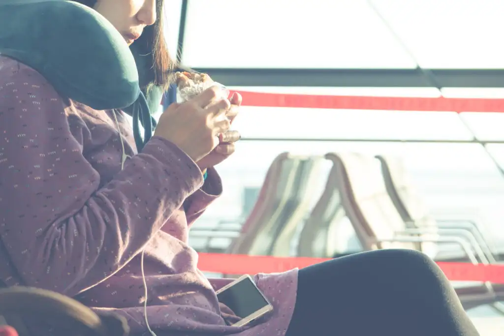 Close up of woman eating a breakfast sandwich and wearing an airplane pillow in an airport