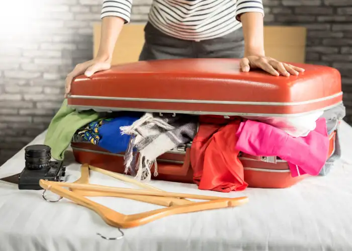 Close up of a person trying to close an overly full suitcase