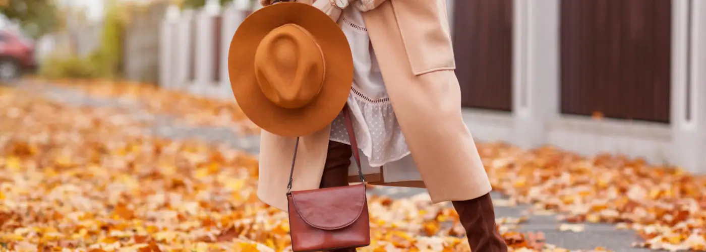 Woman dressed in warm autumn clothes on a street covered with fallen orange leaves