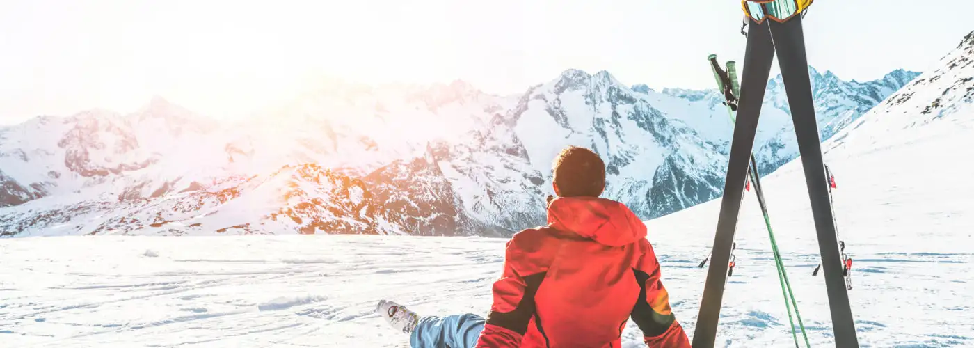 Man sitting next to ski poles looking at mountains