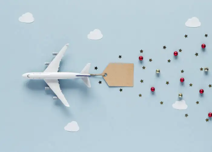 A toy plane on a blue backdrop attached to a tag with small Christmas ornaments trailing behind it