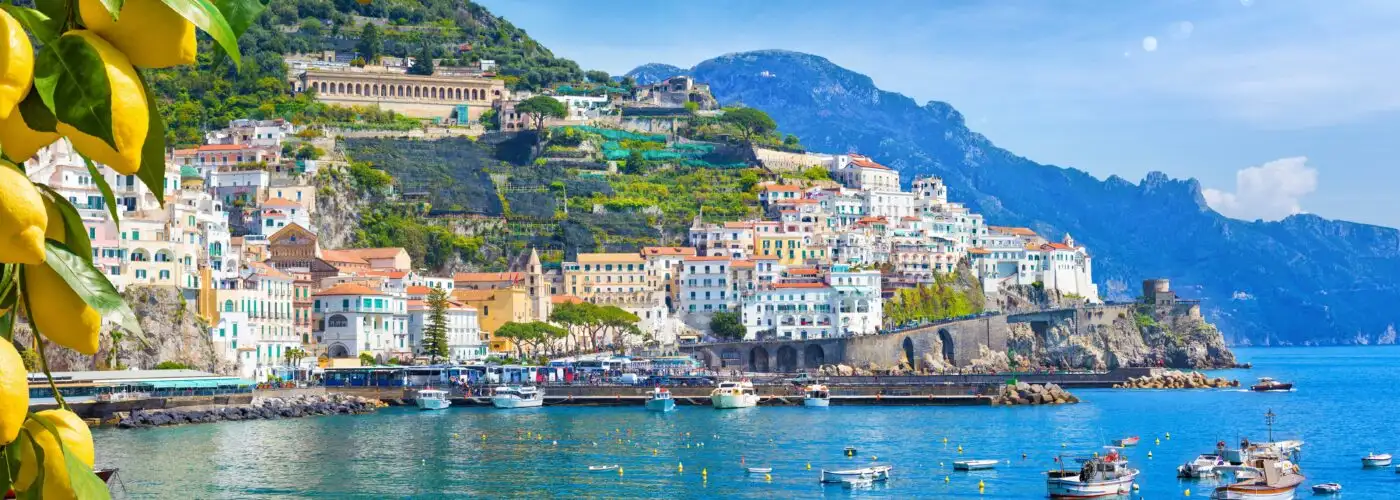 Panoramic view of beautiful Amalfi on hills leading down to coast, Campania, Italy. Amalfi coast is most popular travel and holiday destination in Europe. Ripe yellow lemons in foreground.