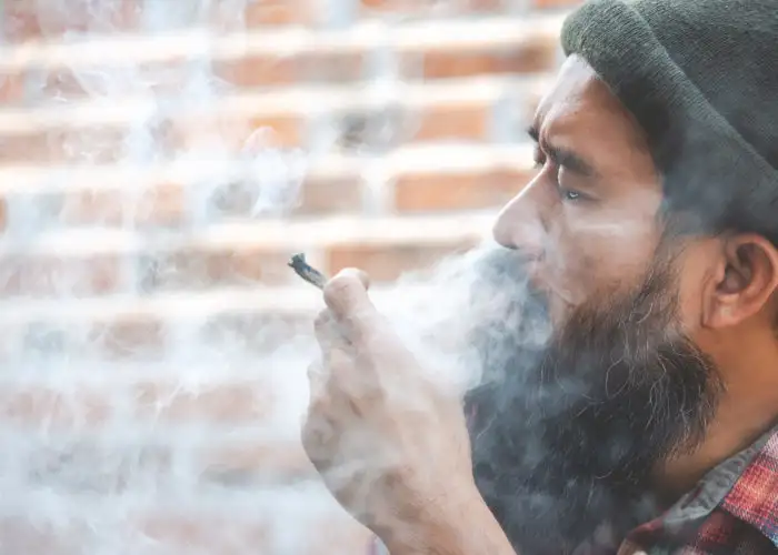 Man smoking a marijuana joint in front of a brick wall