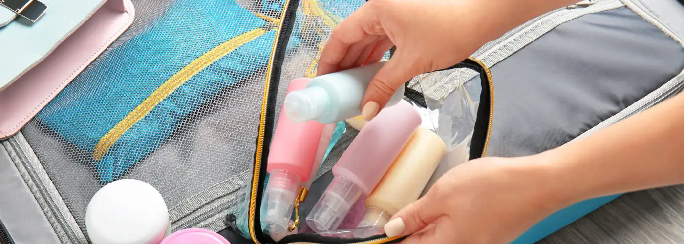 Close up of person packing a clear toiletry bad in a carry-on suitcase