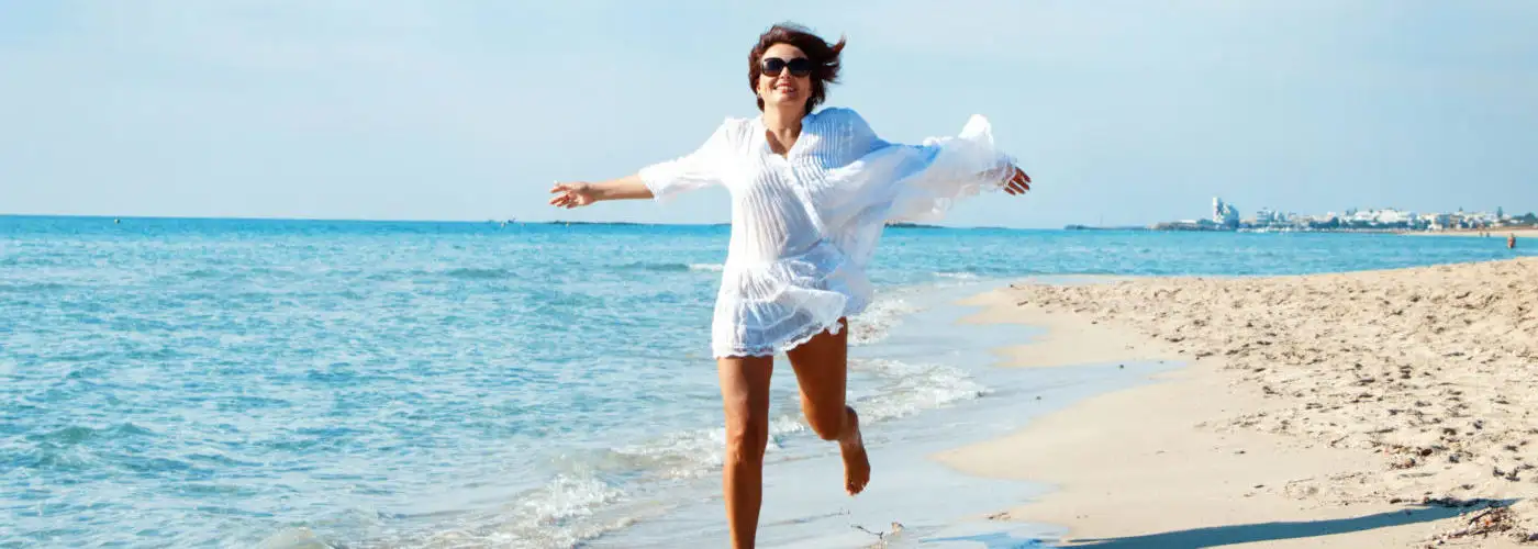 Woman running toward camera on beach in white beach cover up