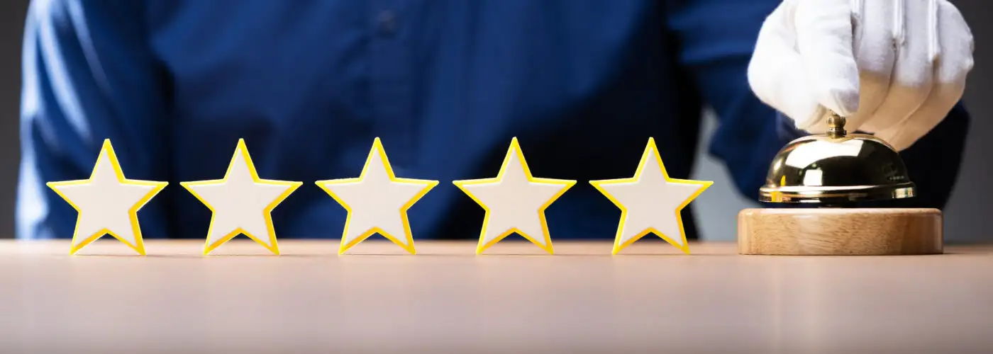 Five wooden stars lined up on a table next to a bell, which is being rung by a hotel worker in white gloves