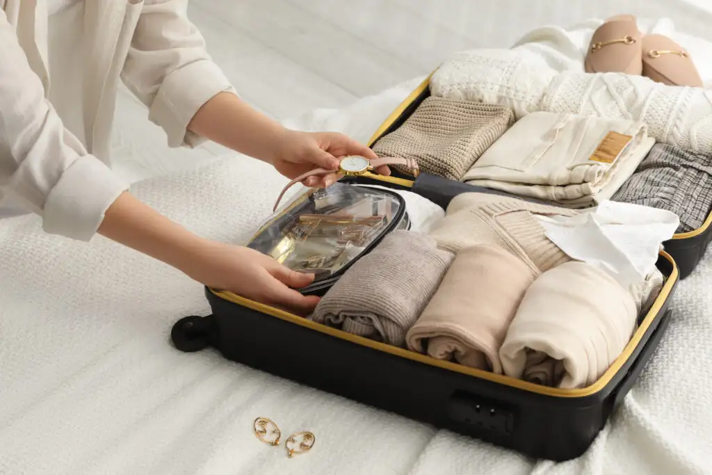 Close up of person packing a small suitcase on top of bed