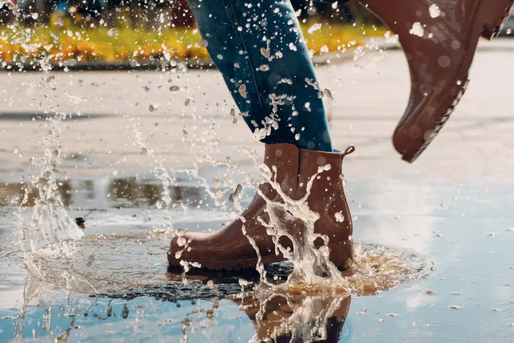 Close up of person wearing brown Chelsea boots and splashing through a deep puddle