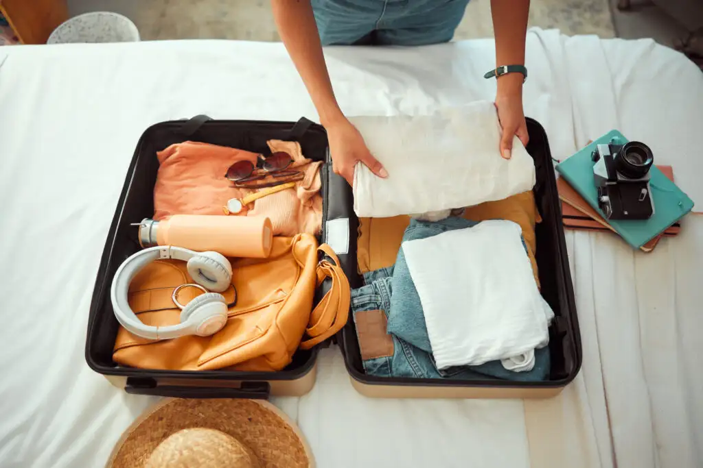 Overhead view of person packing a suitcase with clothes and electronics