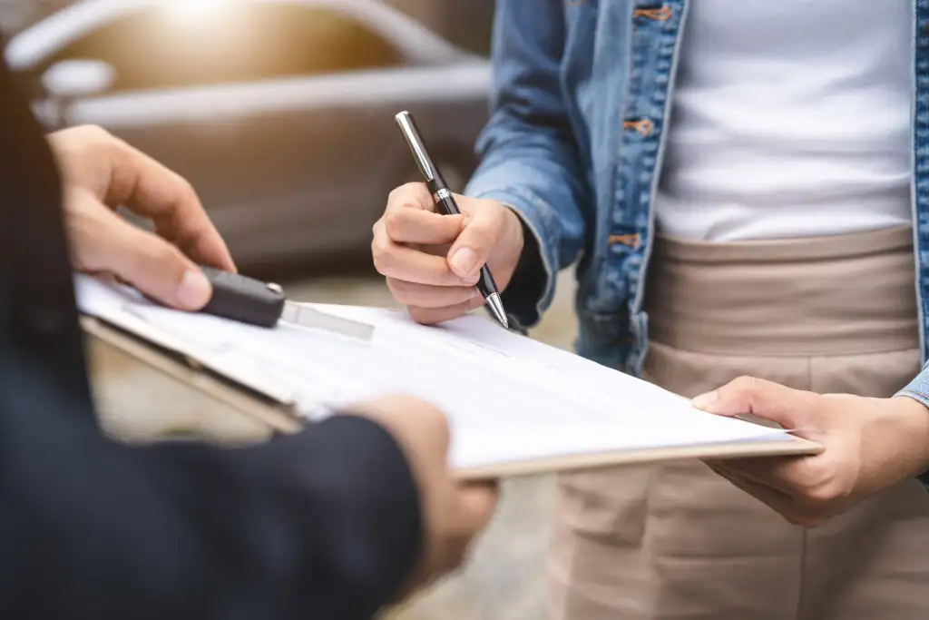 Person signing car insurance paperwork on a clipboard