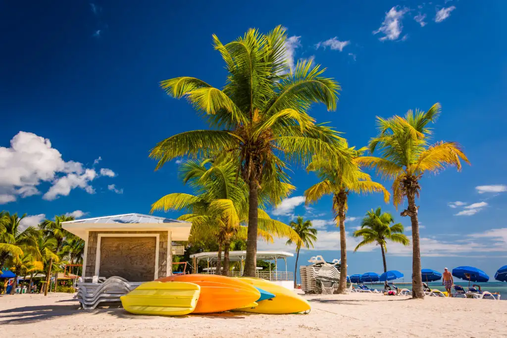 A building, palm trees, and a boat pulled up on the beach in the Florida Keys on a sunny day