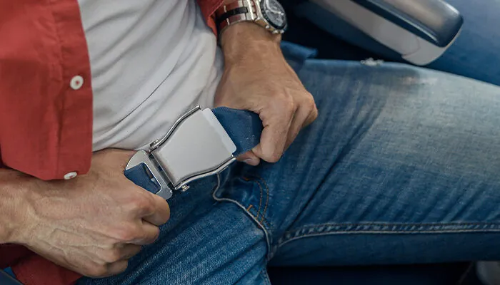 High angle view of male passenger fastening seat belt while sitting on the airplane for safe flight. Safety, traveling concept
