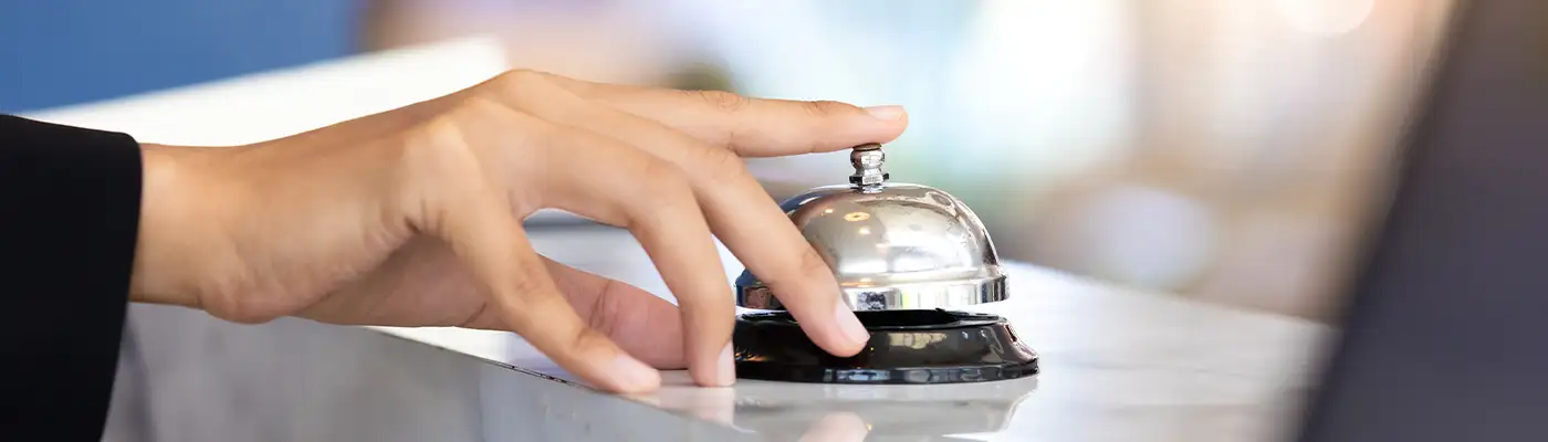 Close up of person's hand ringing front desk check in bell