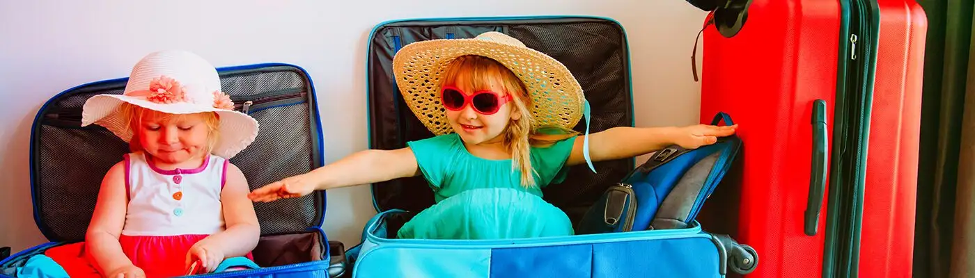 Children playing inside suitcases next to packed luggage