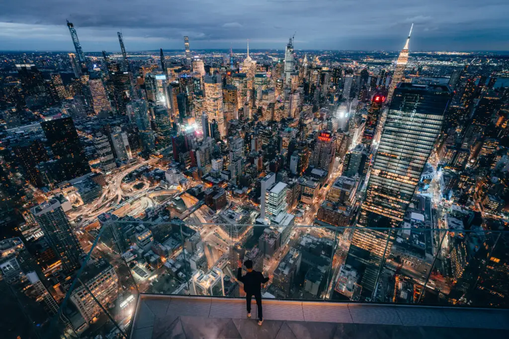 Person looking out the glass walls on The Edge observation deck in New York City at night