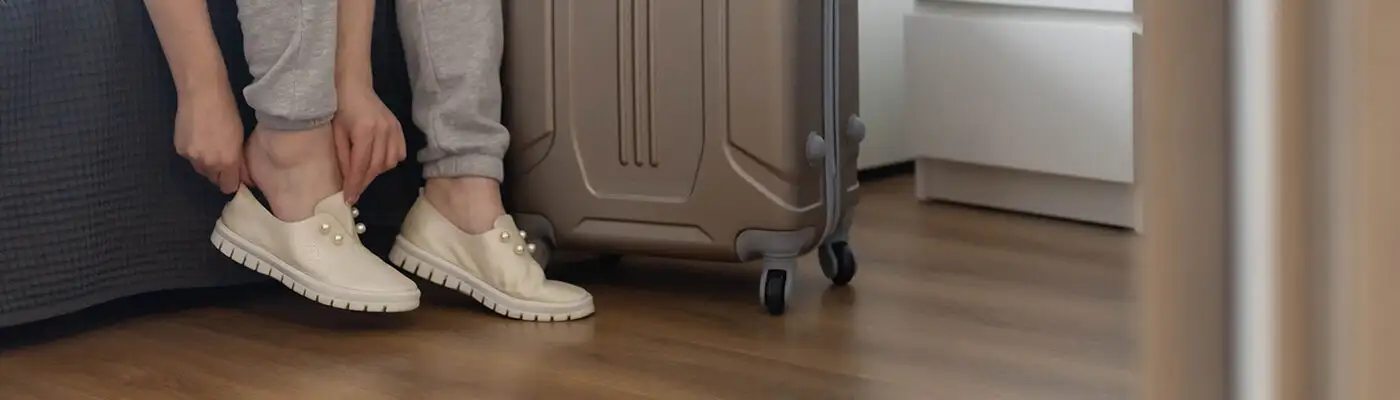 Close up of person putting on shoes next to rolling luggage