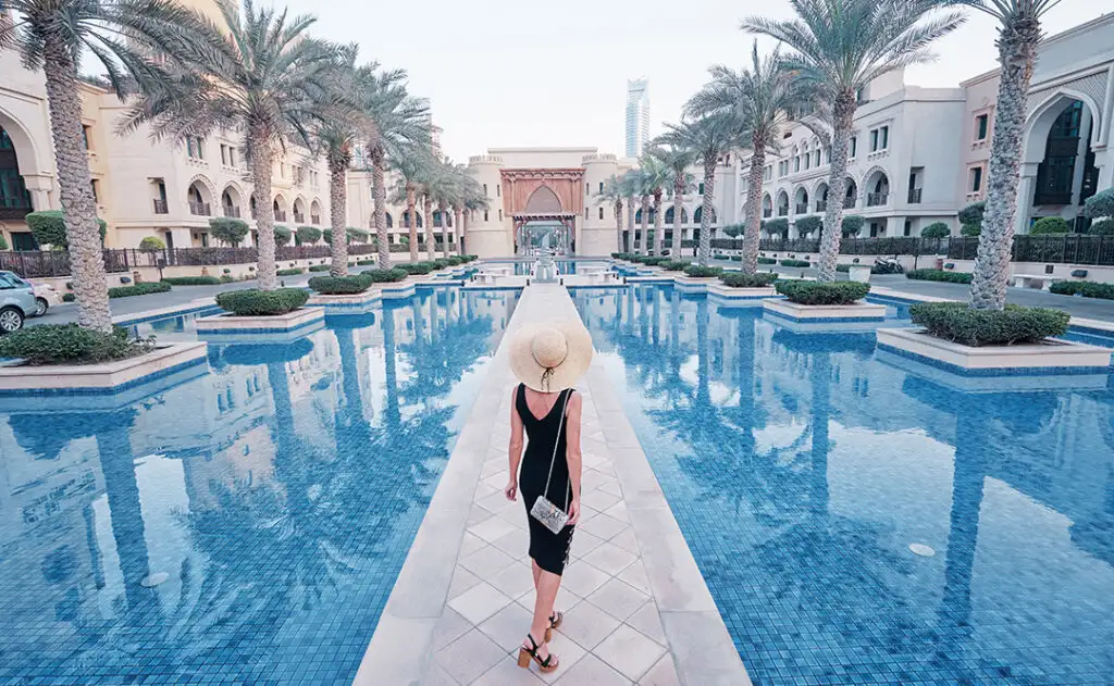 Beautiful young woman in black dress with hat walking on Dubai Downtown.