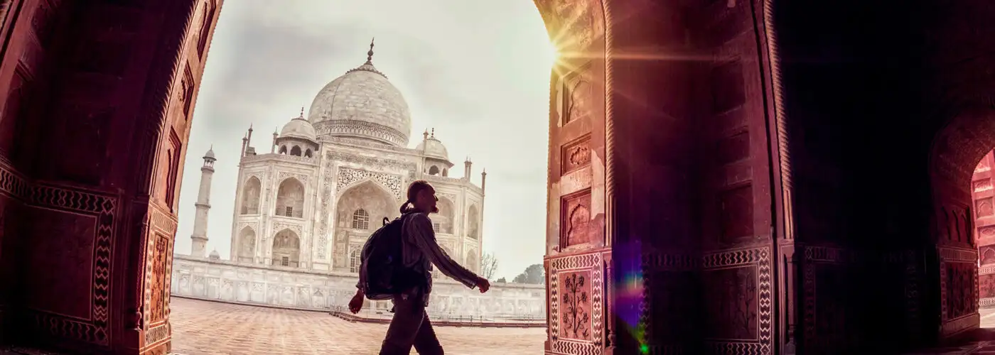 Tourist with backpack walking in the mosque arch near Taj Mahal in Agra