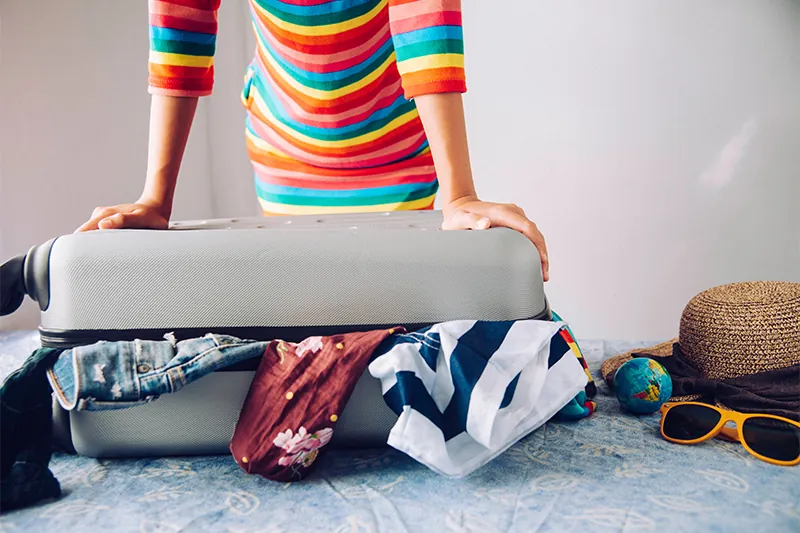 Close up of person in colorful striped dress trying to close an overflowing suitcase