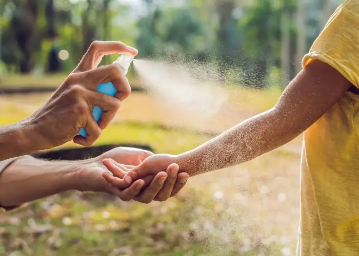 parent spraying mosquito repellent on child.