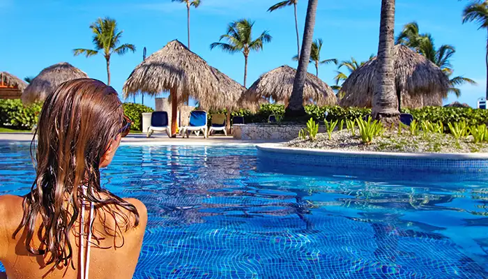 Woman in pool surrounded by palm trees and umbrellas