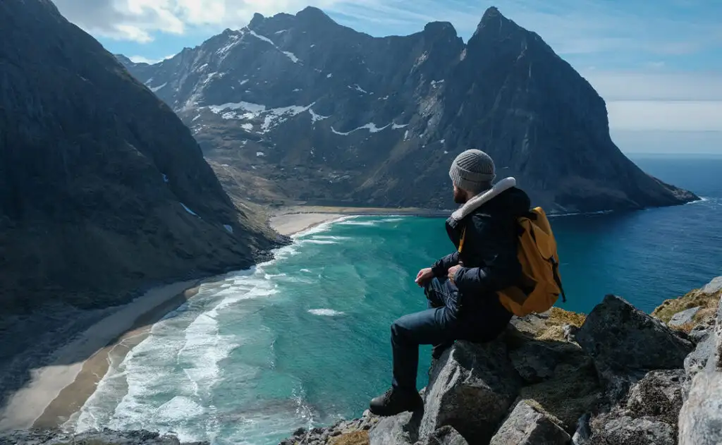 Man sitting on cliff edge alone enjoying aerial view backpacking lifestyle travel adventure outdoor vacations in Norway top of Reinebringen mountain.